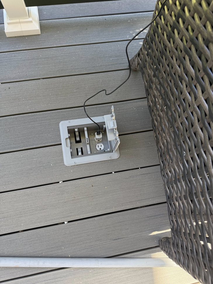 An open outdoor floor outlet with a cable plugged in on a wooden deck, installed by Watts Up Electric LLC in Summerville, SC.