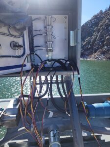 An open outdoor electrical box with wiring, overlooking a body of water, installed by Trademark Elite Electrical Services in Butte, MT