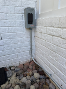 An outdoor electrical conduit and box professionally installed on a white brick wall by C.M.S Electrical in Staley, NC.