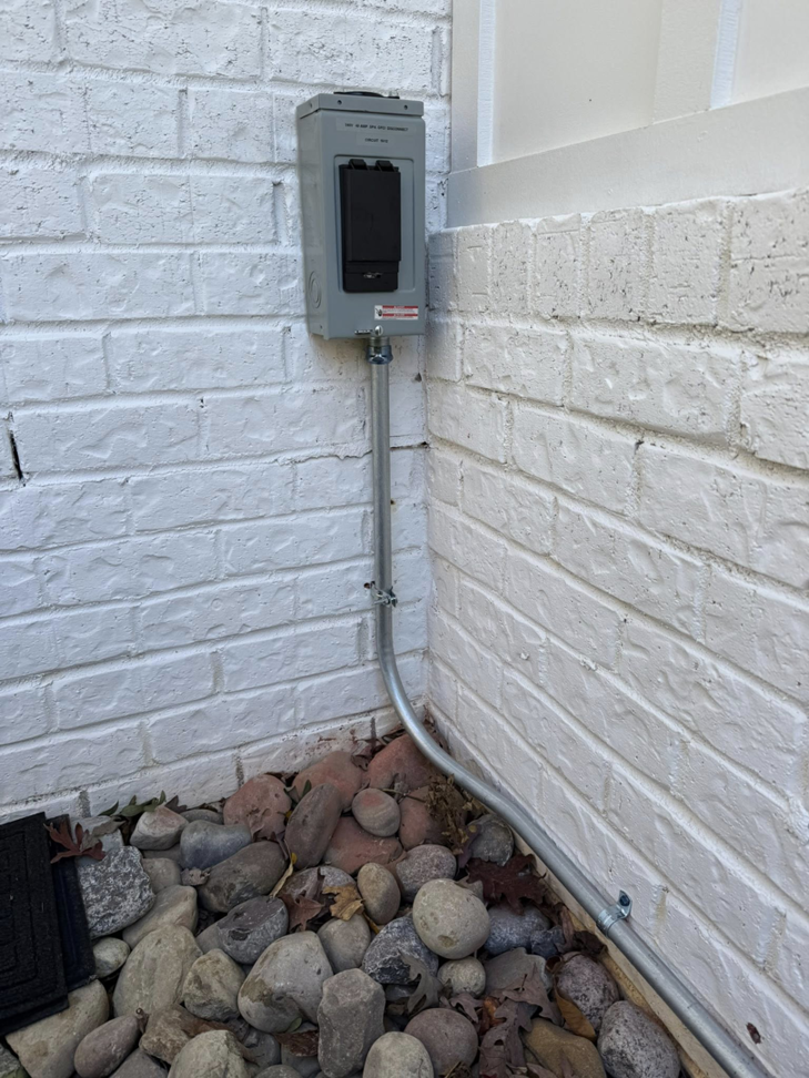An outdoor electrical conduit and box professionally installed on a white brick wall by C.M.S Electrical in Staley, NC.