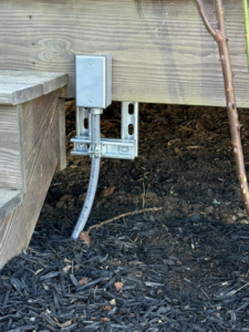An outdoor electrical conduit and box installed under a wooden deck by C.M.S Electrical in Staley, NC.