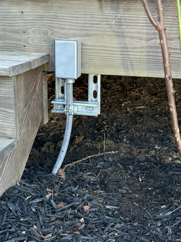 An outdoor electrical conduit and box installed under a wooden deck by C.M.S Electrical in Staley, NC.