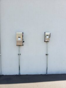 Two outdoor electrical disconnect boxes installed on a white exterior wall by TJS Electrical Services Inc in Mesa, AZ.