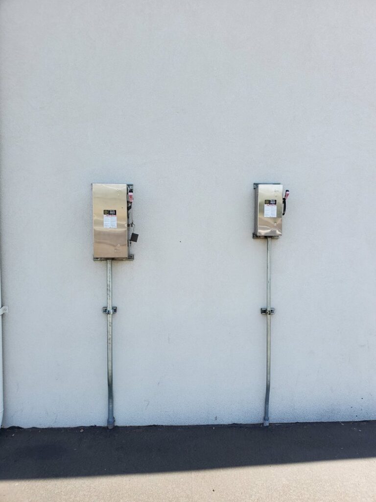 Two outdoor electrical disconnect boxes installed on a white exterior wall by TJS Electrical Services Inc in Mesa, AZ.