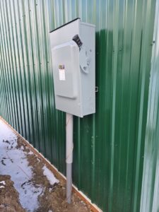 An outdoor electrical disconnect switch installed on a green corrugated wall by Trademark Elite Electrical Services in Butte, MT