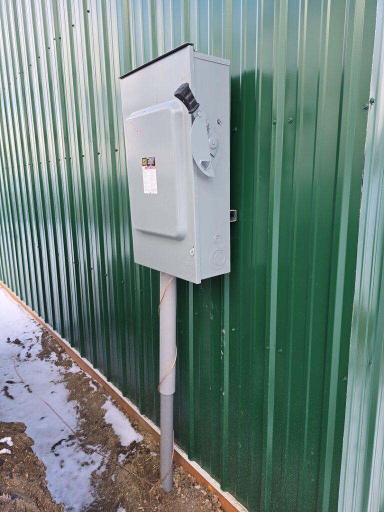 An outdoor electrical disconnect switch installed on a green corrugated wall by Trademark Elite Electrical Services in Butte, MT