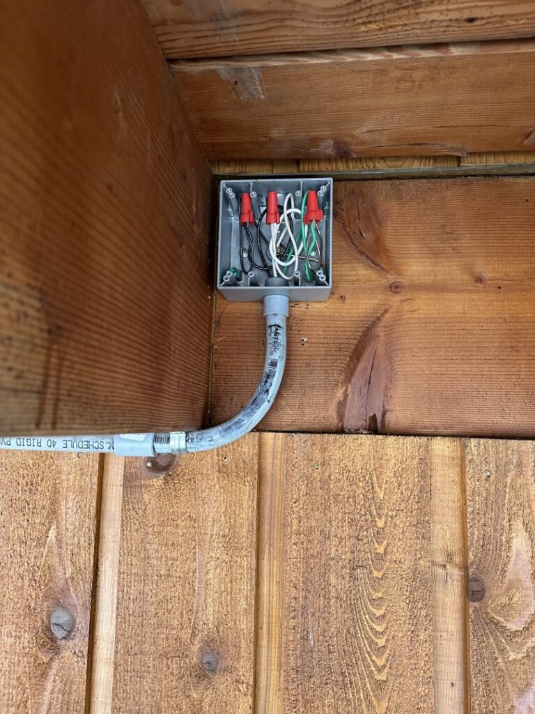 An outdoor electrical junction box with conduit and wiring installed on a wooden wall by Sunrise Electric LLC in Kalispell, MT.