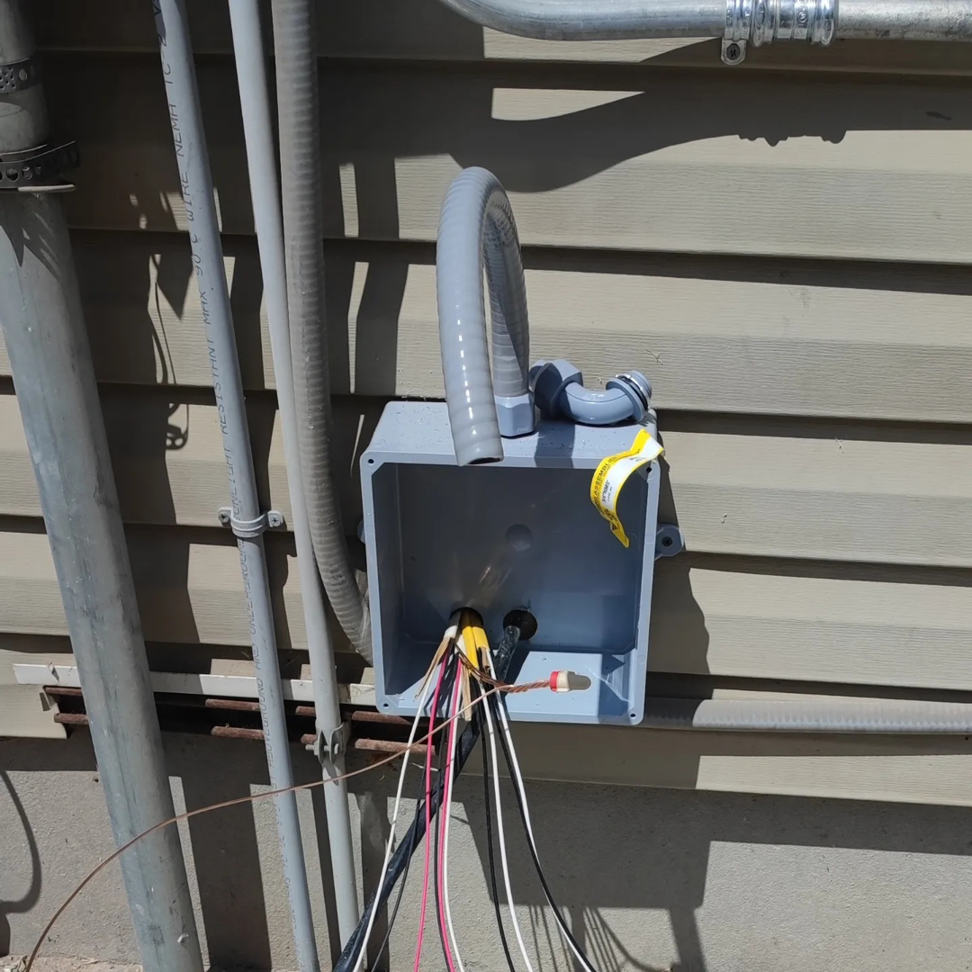 An outdoor electrical junction box with wires and conduits on the side of a building by Lara Electric in Miami, FL.