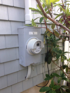 An outdoor electrical meter box with conduit and wiring installed on a gray shingle wall by RightWay Electric RI in Providence, RI.