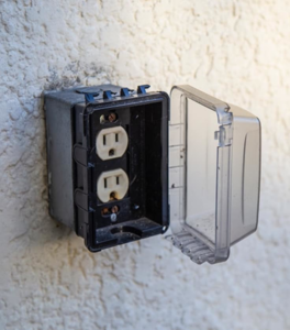 An outdoor electrical outlet with a weatherproof cover installed on a textured wall by Dmac Electric in Detroit, MI