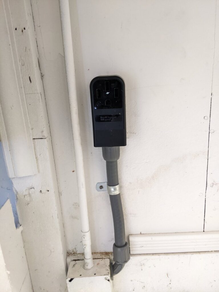 An outdoor electrical outlet and conduit installed on a white exterior wall by Jeremy Electrical in Roeland Park, KS.