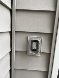 An outdoor electrical outlet with a weather-resistant cover installed on house siding by Mister Sparky Kansas City, MO.