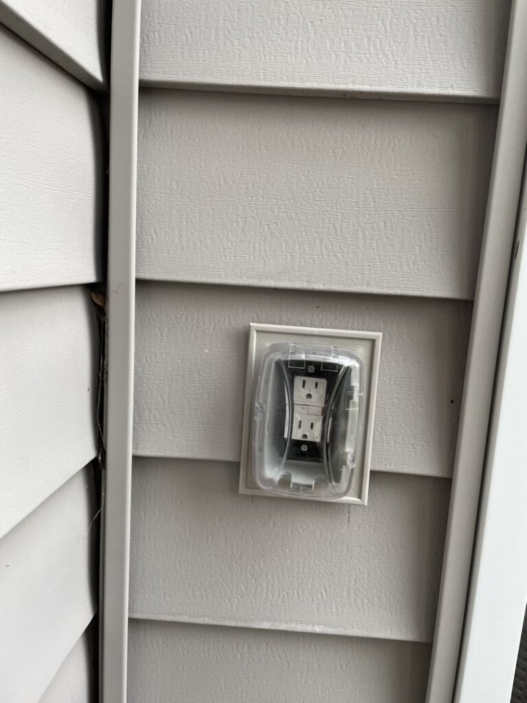 An outdoor electrical outlet with a weather-resistant cover installed on house siding by Mister Sparky Kansas City, MO.