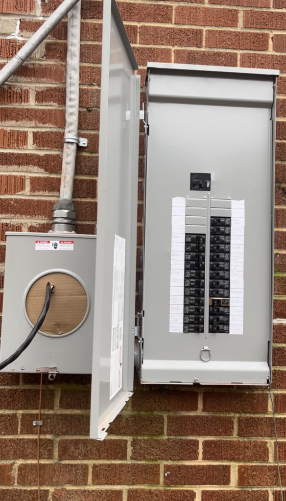 An outdoor electrical panel and meter base installed on a brick wall by CJ Lighting Solution LLC in Greensboro, NC.