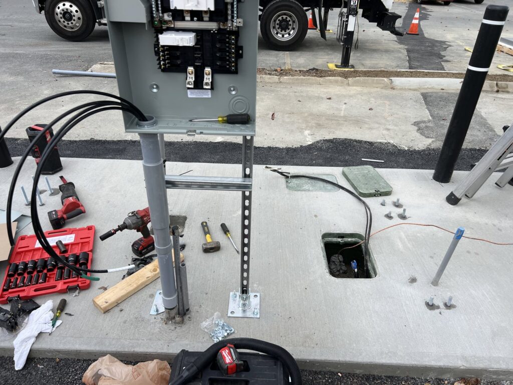 An outdoor electrical panel installation with conduits and tools on the ground, performed by Peeler Electric Light & Power in Merrimack, NH.
