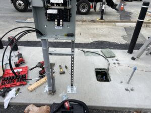 An outdoor electrical panel installation with conduits and tools on the ground, performed by Peeler Electric Light & Power in Merrimack, NH.