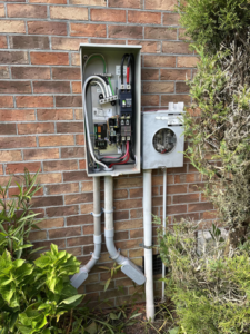 An outdoor electrical panel and meter box on a brick wall, showing wiring by Strother & Son Electric in Mount Pleasant, SC.