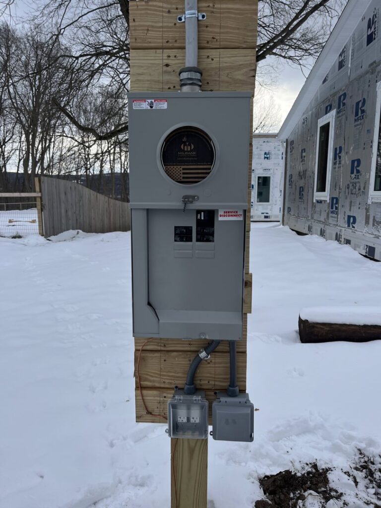 An outdoor electrical service panel mounted on a wooden post in a snowy landscape, installed by Greif Electric Company in Dolgeville, NY.