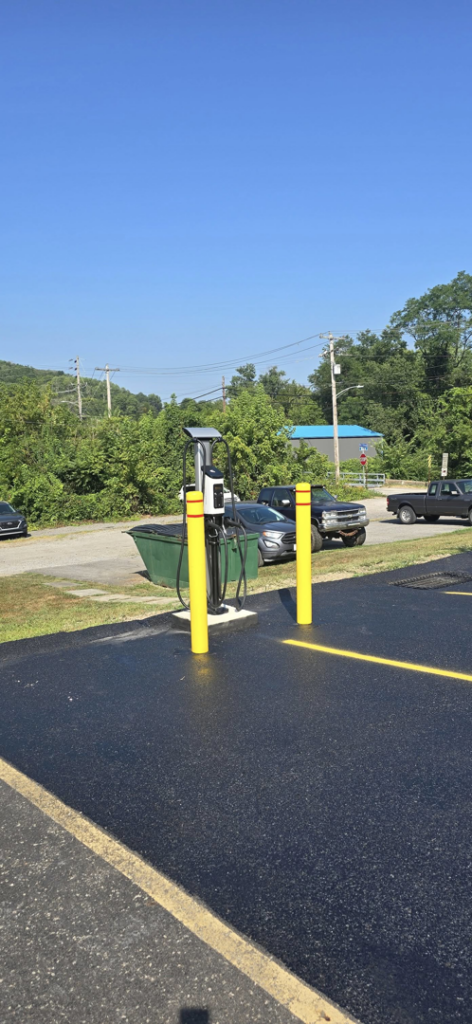 An outdoor electric vehicle charging station with yellow bollards under a clear sky by Pittsburgh Electric & Maintenance in Pittsburgh, PA