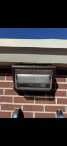 An outdoor floodlight installation on a brick wall with a ladder, by Delta Current Electric in Jonesboro, AR.