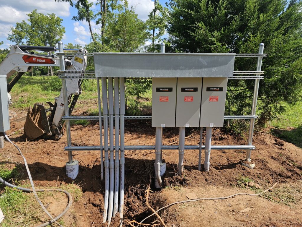 Outdoor Generac electrical panel and conduit installation with an excavator in the background by Powered Electrical & Lighting Services LLC in Springfield, MO.