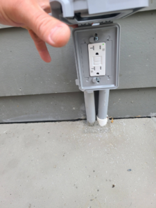 A hand inspecting an outdoor GFCI electrical outlet installed by Joe Does It-Electrical Services in Atlanta, GA.