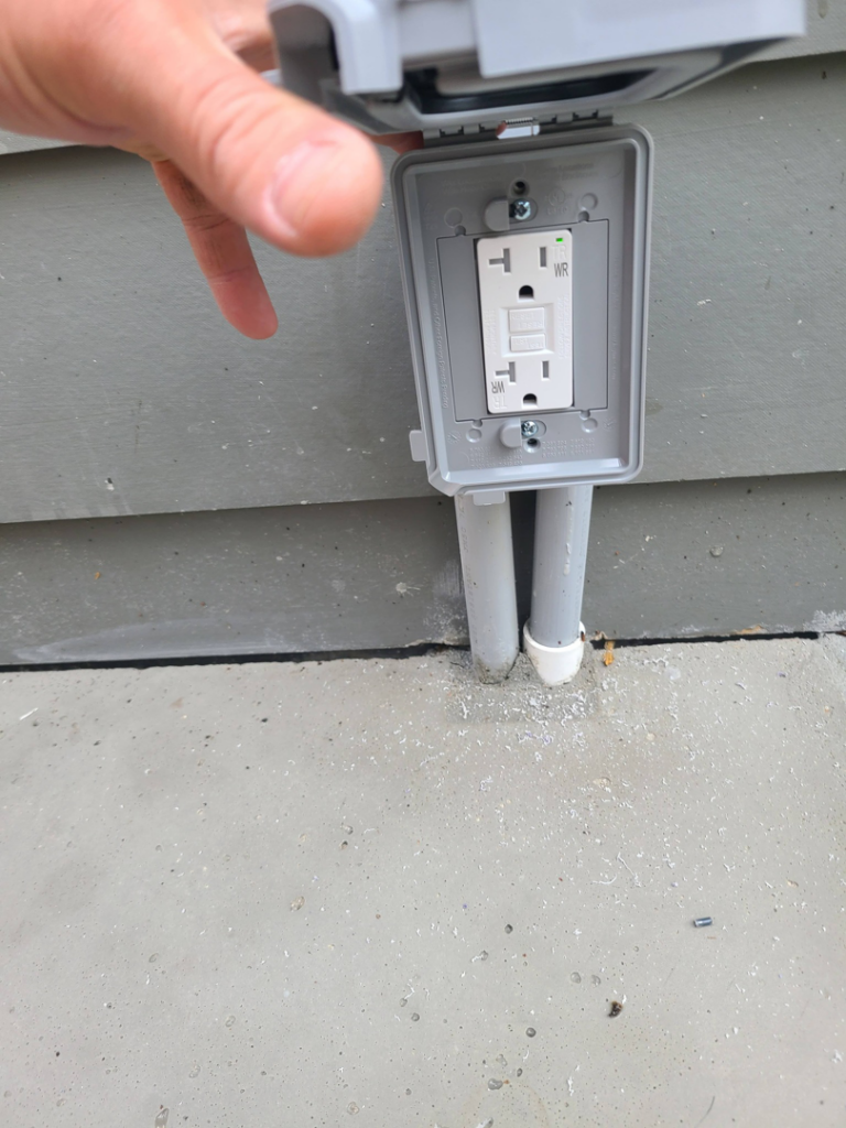 A hand inspecting an outdoor GFCI electrical outlet installed by Joe Does It-Electrical Services in Atlanta, GA.