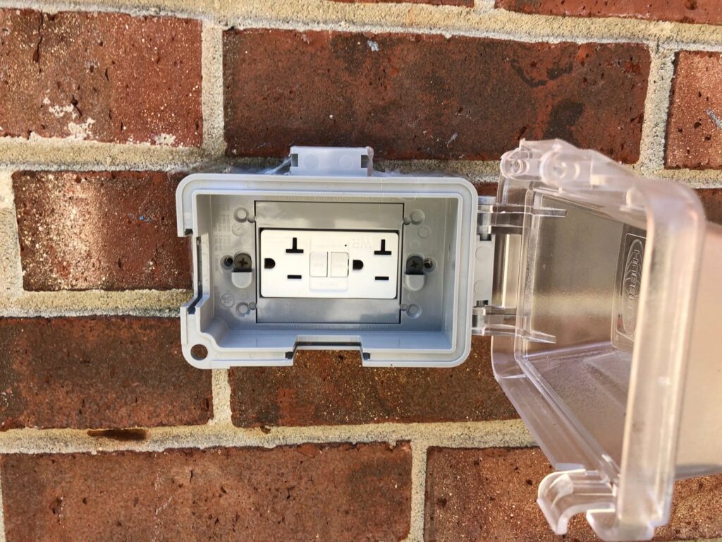 An outdoor GFCI outlet with a weatherproof cover installed on a brick wall by McCall Enterprises in Atlanta, GA.