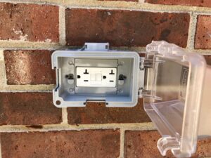 An outdoor GFCI outlet with a weatherproof cover installed on a brick wall by McCall Enterprises in Atlanta, GA.