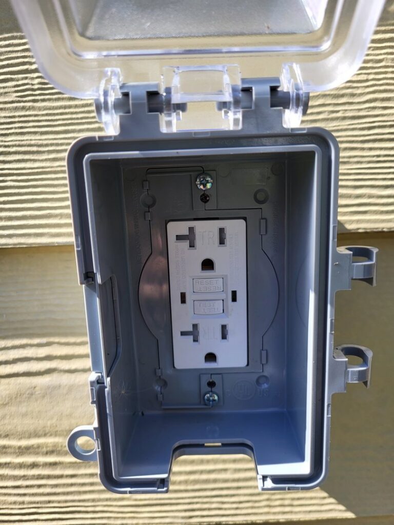 An outdoor GFCI outlet with an open weatherproof cover, installed by Ozzy Electric in Jacksonville, FL.