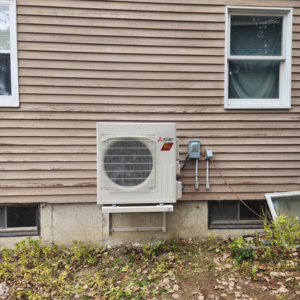 An outdoor heat pump condenser unit installed on the side of a house by Element Heat Pumps in Gray, ME.