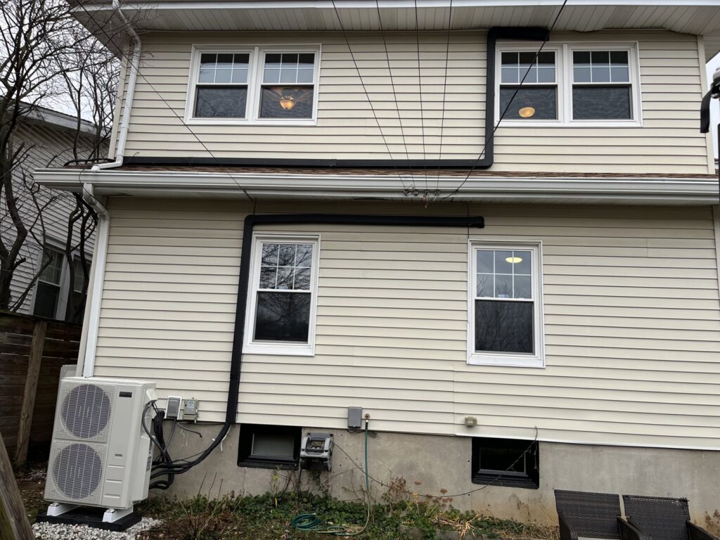 An outdoor heat pump condenser unit with refrigerant lines installed on the side of a house by GrinHouse HVACR in La Grange, KY.