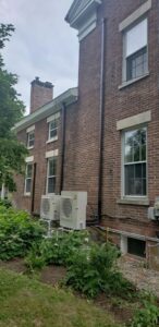 Two outdoor heat pump units installed on the side of a brick building by Superior CO-OP HVAC in Cambridge, NY.