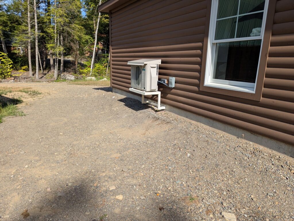 An outdoor heat pump unit installed on the side of a house by Kinney Family Heat Pumps in Augusta, ME.
