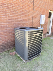 An outdoor HVAC condenser unit installed next to a brick wall by Affordable heating and air conditioning in Meridian, MS.