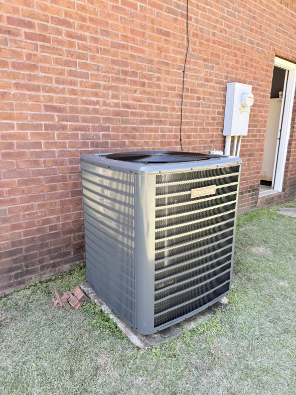 An outdoor HVAC condenser unit installed next to a brick wall by Affordable heating and air conditioning in Meridian, MS.