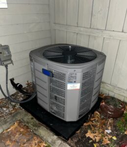 An outdoor HVAC condenser unit installed in a corner next to a house by Joe's Heating & Air Repair LLC in Surf City, NC