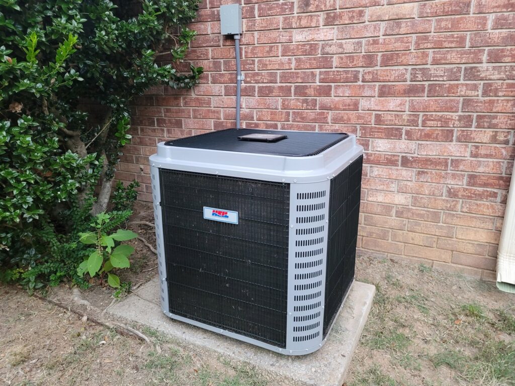 An outdoor HVAC condenser unit installed next to a brick wall by Fusion Heat and Air in Fort Smith, AR.