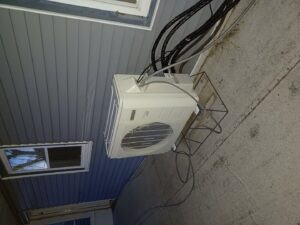 An outdoor HVAC condenser unit installed on a metal frame next to a house by Jones Heating and Refrigeration in Dickinson, ND.