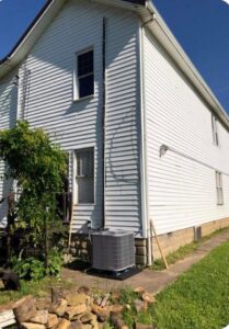 An outdoor HVAC condenser unit installed next to a white residential building by Eastern Air Flow of Kentucky in Richmond, KY.