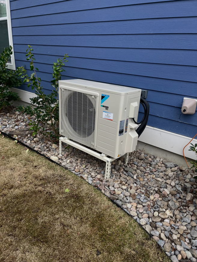 An outdoor Daikin HVAC condenser unit installed next to a blue house by Joe's Heating & Air Repair LLC in Surf City, NC