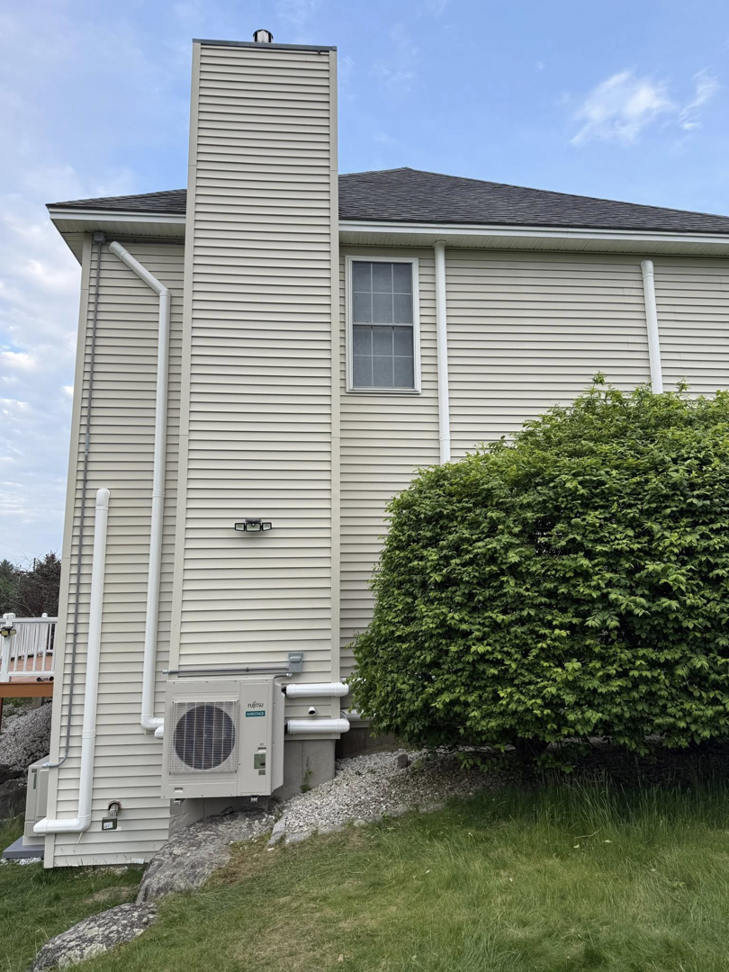 An outdoor HVAC condenser unit installed next to a house by Precision Heating and Gas Service in Derry, NH