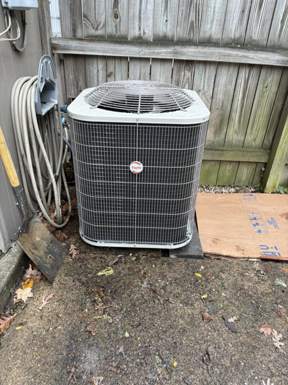 An outdoor Payne HVAC condenser unit installed next to a wooden fence by Pepper Mechanical in Pittsburgh, PA
