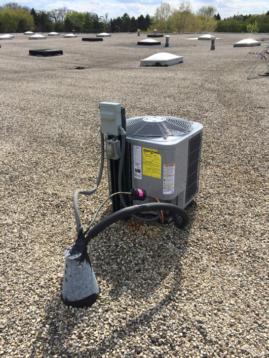 An outdoor HVAC condenser unit installed on a gravel rooftop by Corbe Heating and Air Conditioning in Elgin, IL.