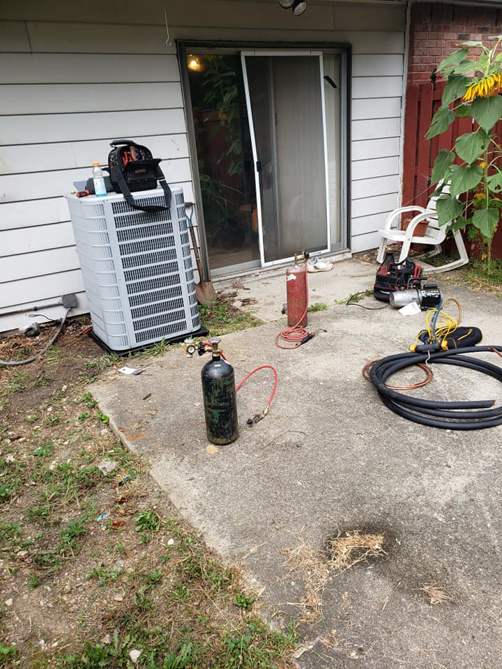 An outdoor HVAC condenser unit being serviced with tools and refrigerant tanks by Kopetsky HVAC in Indianapolis, IN.
