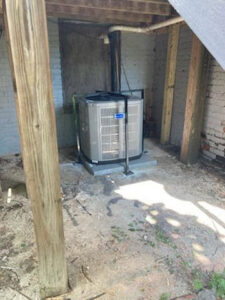 An outdoor HVAC condenser unit installed on a concrete pad under a house by Tack Mechanical LLC in Baltimore, MD.