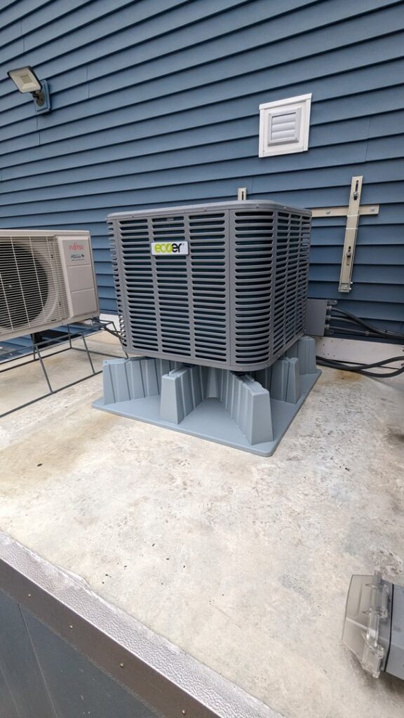 An outdoor HVAC condenser unit installed on a concrete pad next to a residential building by WARM Global HVAC in East Providence, RI.