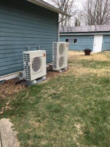 Two outdoor HVAC condenser units installed next to a residential building by Commercial Service in Bloomington, IN.