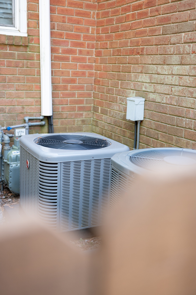 Two outdoor HVAC condenser units installed next to a brick house by Travis Crawford Heating, Cooling, Plumbing & Electrical in Charlotte, NC.
