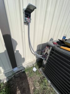 An outdoor electrical disconnect box and exposed wiring on an HVAC unit, showing electrical service by Quistian Lighting in Arlington, TX